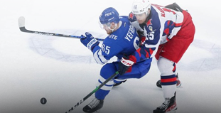 Хоккеисты двух команд в моменте игры на льду. Игрок в синей форме ведет шайбу, его преследует хоккеист в бело-красной форме. Наступательная динамика и интенсивность матча видны по их позам и вниманию к игре